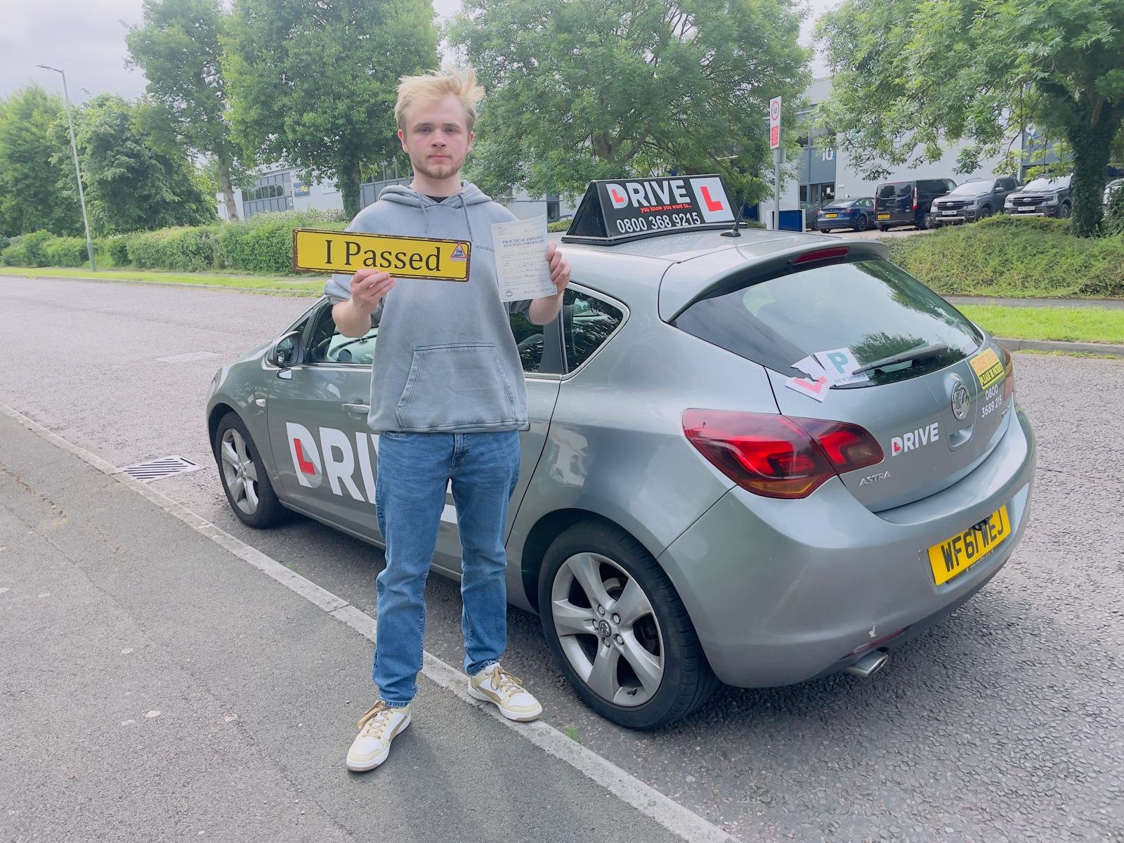 Anthony holding an I Passed sign beside a JM Drive car